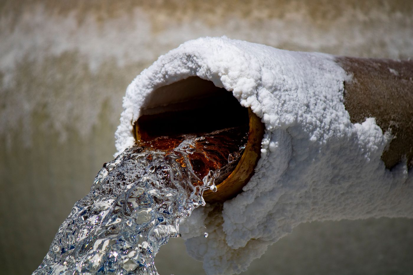 Water gushing from a rusty pipe end crusted with ice